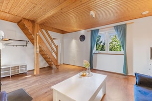 A room with a wooden staircase, a white table, a window with curtains, and a clock on the wall. - Comfortable Holiday Home With a Fireplace (Darlowo)
