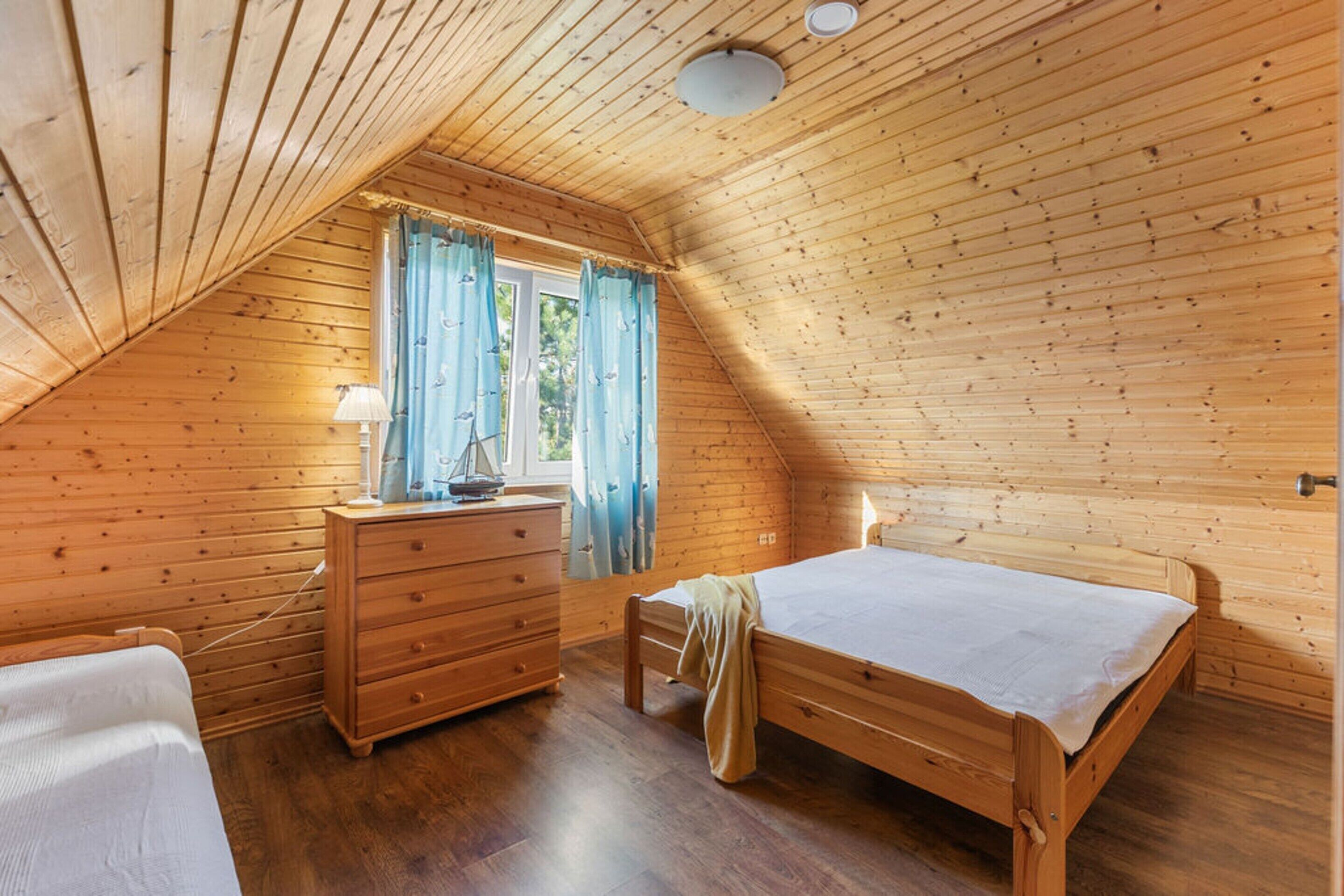 A cozy attic bedroom with a wooden sloped ceiling, a single bed, a dresser, and a window with curtains.