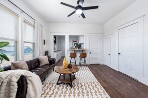 A modern living room with a brown leather sofa, a round wooden coffee table, and a ceiling fan. - Coastal Sophistication (Galveston)