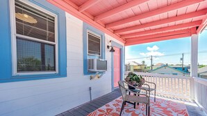 A covered porch with a wooden floor, a chair, and a potted plant. - Coastal Sophistication (Galveston)