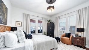 A modern bedroom with a large bed, a seating area, and a view of the outdoors. - Coastal Sophistication (Galveston)