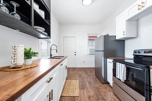 A modern kitchen with white cabinetry, a wooden countertop, a stainless steel refrigerator, and a built-in oven. - Coastal Sophistication (Galveston)