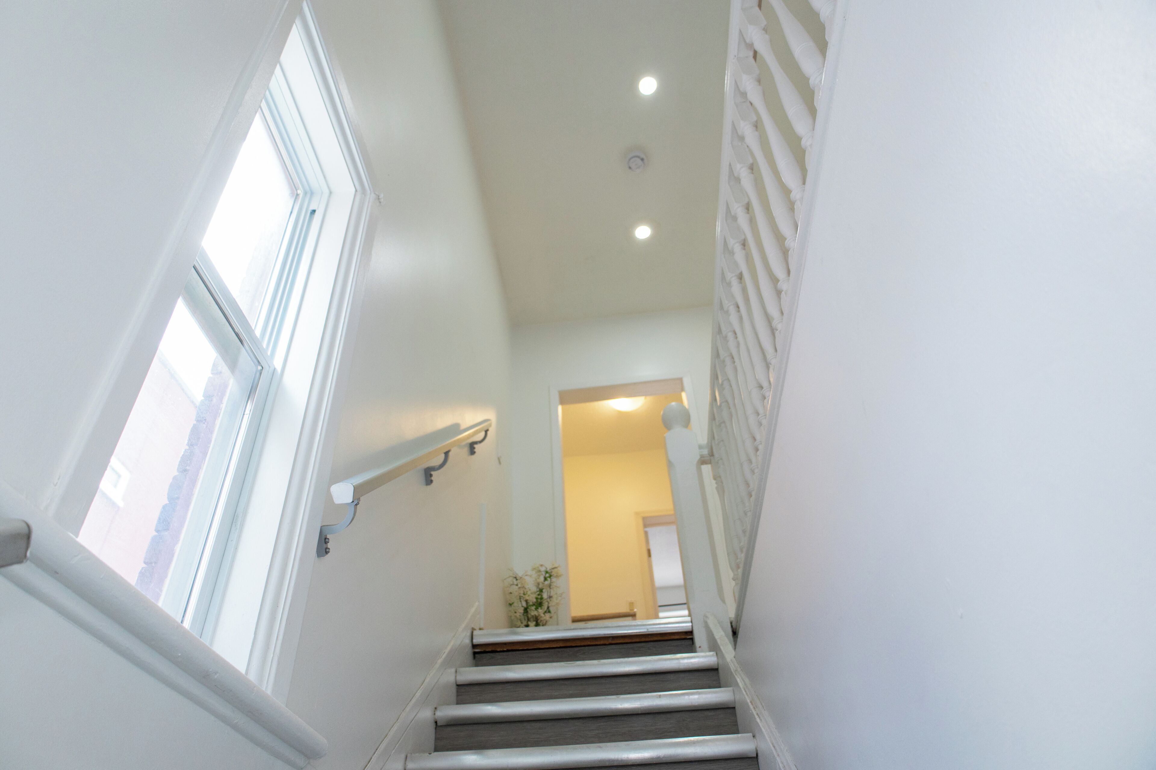 A staircase with white walls and a handrail, leading to a room with a door at the top.