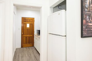 A narrow hallway with a wooden door, a white refrigerator, and a small kitchen area with a microwave. - Charming Stay in the heart of Chinatown. Explore and Have Fun (Ottawa)