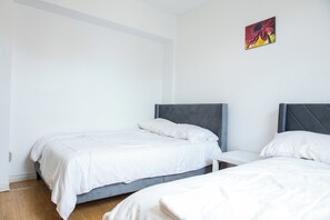 A bedroom with two beds, a small bedside table, and a wall-mounted painting.