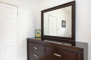 A dark wooden dresser with a large mirror above it, reflecting a white door and a framed picture on the wall.