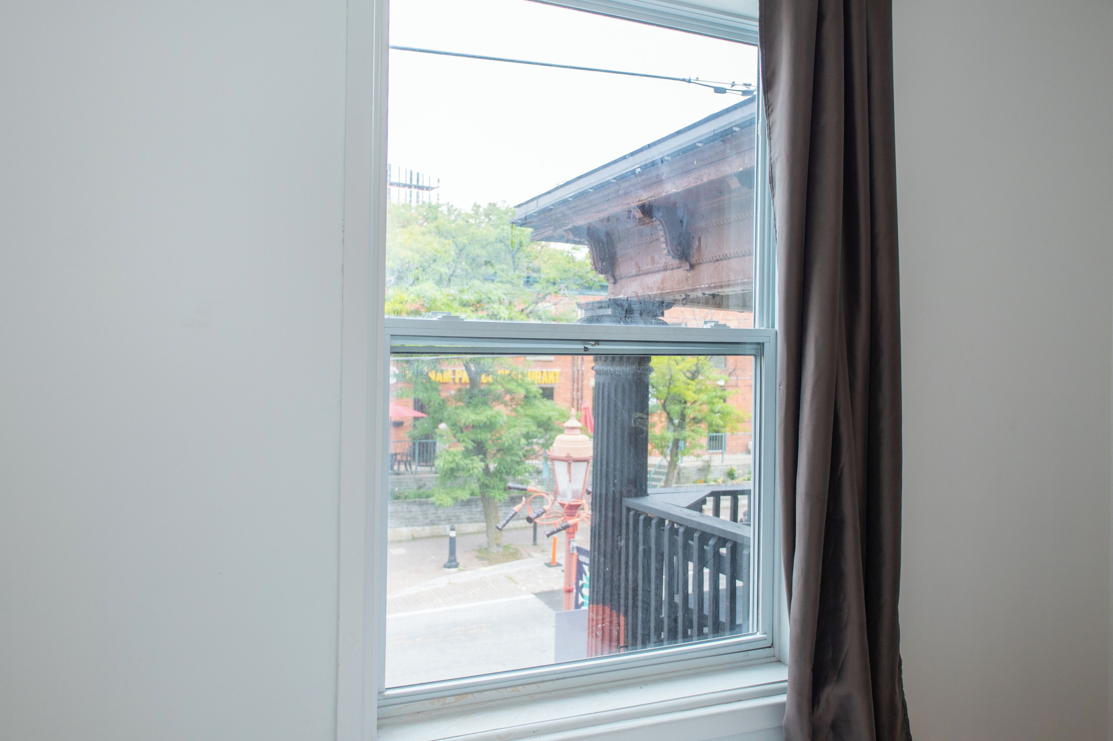 Une fenêtre donnant sur un bâtiment avec des colonnes et un arbre à l’extérieur.