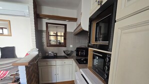 A compact kitchen with white cabinets, a stove, microwave, and a sink. - Charming home in the heart of the Corbières region – Patio, courtyard. (Fabrezan)