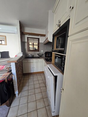 A compact kitchen with white cabinets, a stove, microwave, and a sink. - Charming home in the heart of the Corbières region – Patio, courtyard. (Fabrezan)