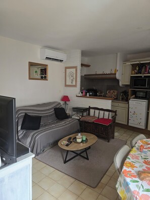 Un espacio habitable compacto con sofá, una mesa de centro, comedor y kitchenette.