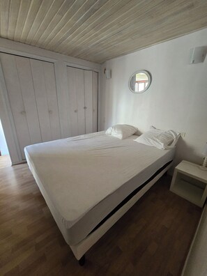 Un dormitorio con cama, mesita de noche, armario y un espejo redondo en la pared.