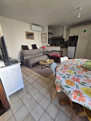 Ein kompakter Wohnbereich mit Bett, kleinem Esstisch, Fernseher und Küchenzeile.