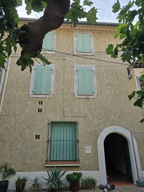 A building facade with green shutters, a visible number '6' on the door, and potted plants at the base. - Charming home in the heart of the Corbières region – Patio, courtyard. (Fabrezan)