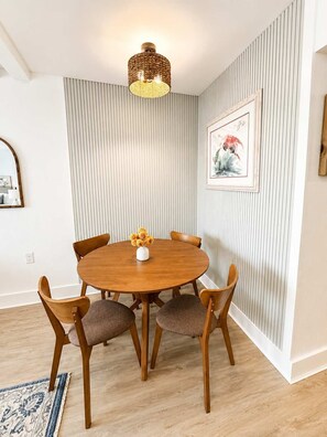 A dining area with a round wooden table, six chairs, a vase with flowers, a hanging light fixture, a framed artwork, and a mirror on the wall. - Oceanfront Serenity at Yachtsman S804 (Myrtle Beach)