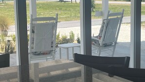 Vista de um quarto com porta de vidro que dá para uma varanda com duas cadeiras brancas e uma pequena mesa.