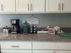 En köksbänk med en kaffebryggare, en vattenautomat, ett ställ för kaffemuggar och en skylt som visar att det finns kaffe, te och kakao att tillgå.
