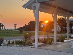 A covered outdoor area with a view of the sunset over the ocean, a stop sign, and a grassy area with plants. - Sweeping Gulf View 1 Block to the Beach - 1 Level Retreat in Mexico Beach! (Mexico Beach)