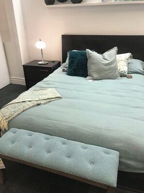 Un lit doté d’une tête de lit capitonnée, d’une lampe de chevet et de plusieurs oreillers.