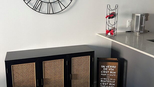 Interior moderno com relógio fixado na parede, adega, máquina de café e armário com painéis de rattan.