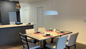 Uma sala de jantar moderna com mesa de madeira, cadeiras estofadas cinzentas e uma luminária pendente.