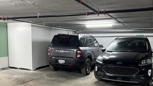 Uma garagem de estacionamento com dois SUVs estacionados, pisos de concreto e tubulações no teto.