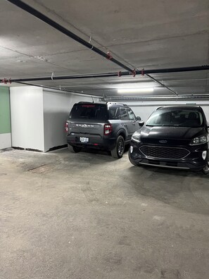 Eine Parkgarage mit zwei SUVs, Betonböden und Rohrleitungen an der Decke.
