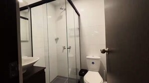 Een moderne badkamer met een douche met glazen wand, een wit toilet en een donkere wastafel.