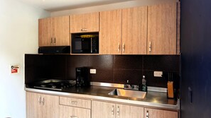 A kitchen with wooden cabinets, a microwave, a gas stove, and a stainless steel sink. - Oasis Penthouse Poblado (Medellín)