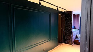 Un couloir avec une porte vert foncé, un mur de marbre et, au fond, on aperçoit une chambre à coucher avec un lit et une table de chevet.