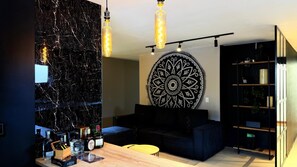 A modern living room with a black marble wall, a round patterned wall hanging, a dark sofa, a wooden coffee table, and a bookshelf. - Oasis Penthouse Poblado (Medellín)