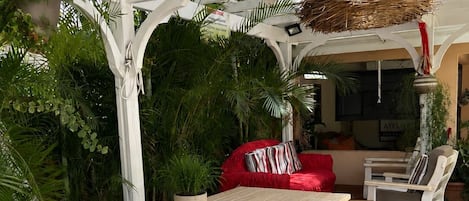 A wooden picnic table with benches, surrounded by lush greenery and a red sofa.