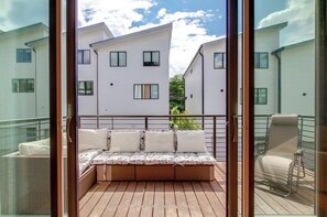 Ein Balkon mit Holzboden, einer gepolsterten Sitzecke und einem Metallstuhl.