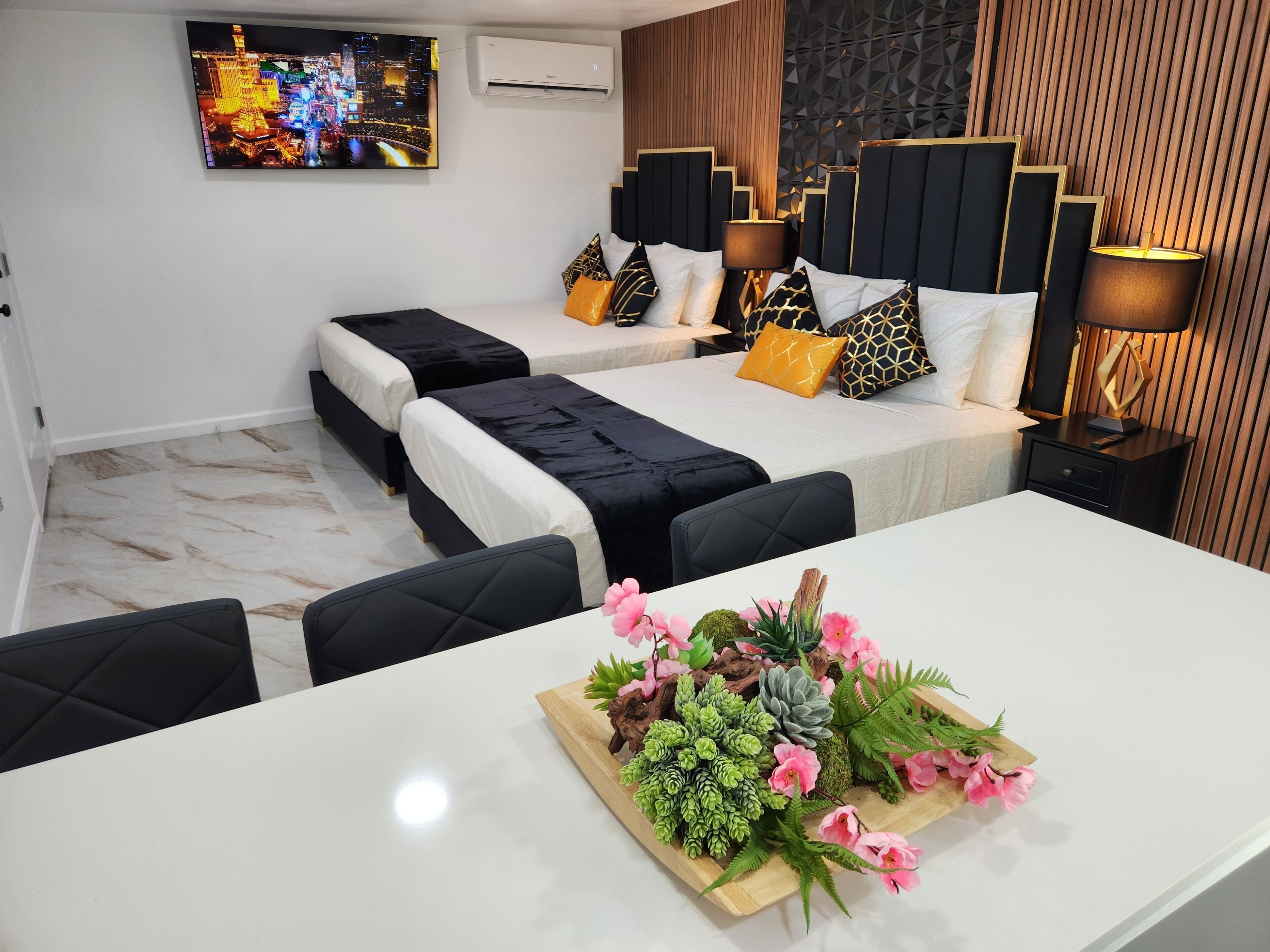 A hotel room with two beds, a TV, a desk, and a decorative plant arrangement.