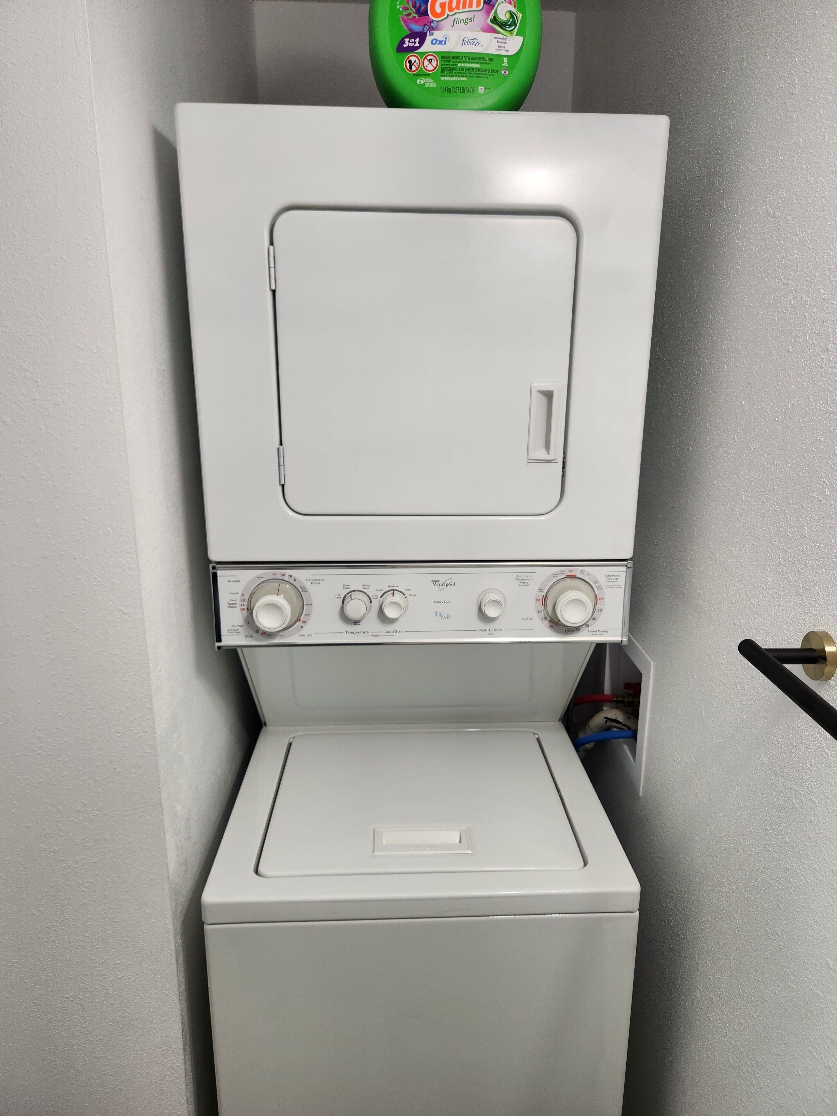A front-loading washer and dryer unit with control knobs and a detergent bottle above.