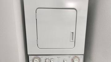 A front-loading washer and dryer unit with control knobs and a detergent bottle above.