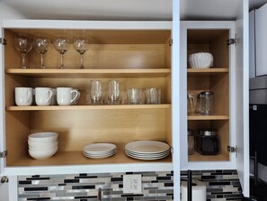 A kitchen cabinet with shelves containing various glassware, cups, and plates.