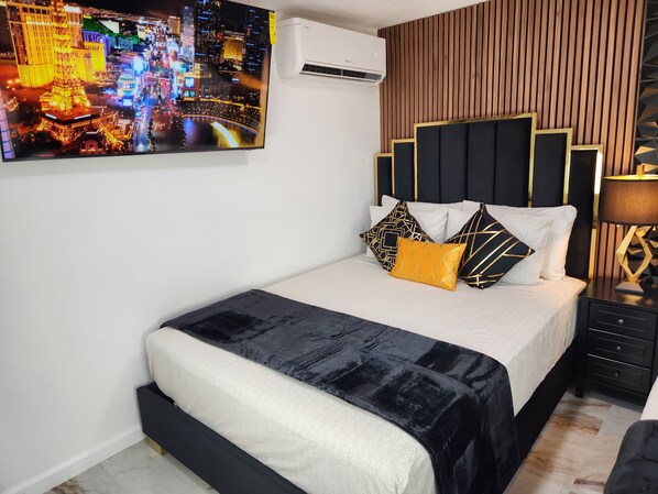 Un dormitorio moderno con cama, mesita de noche, lámpara y una pintura de paisaje urbano en la pared.