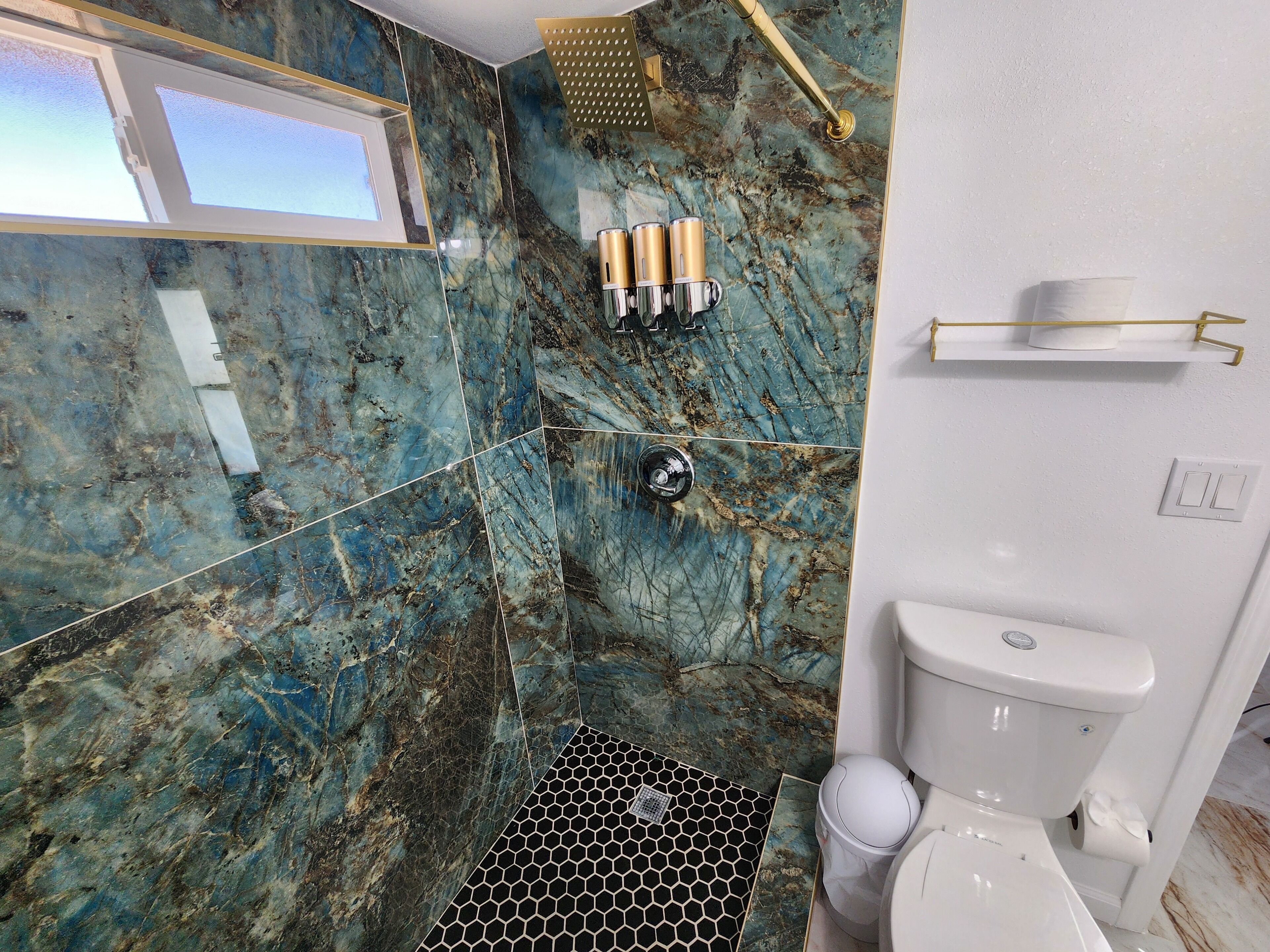 A bathroom with a marble wall, a shower, a toilet, and a window.