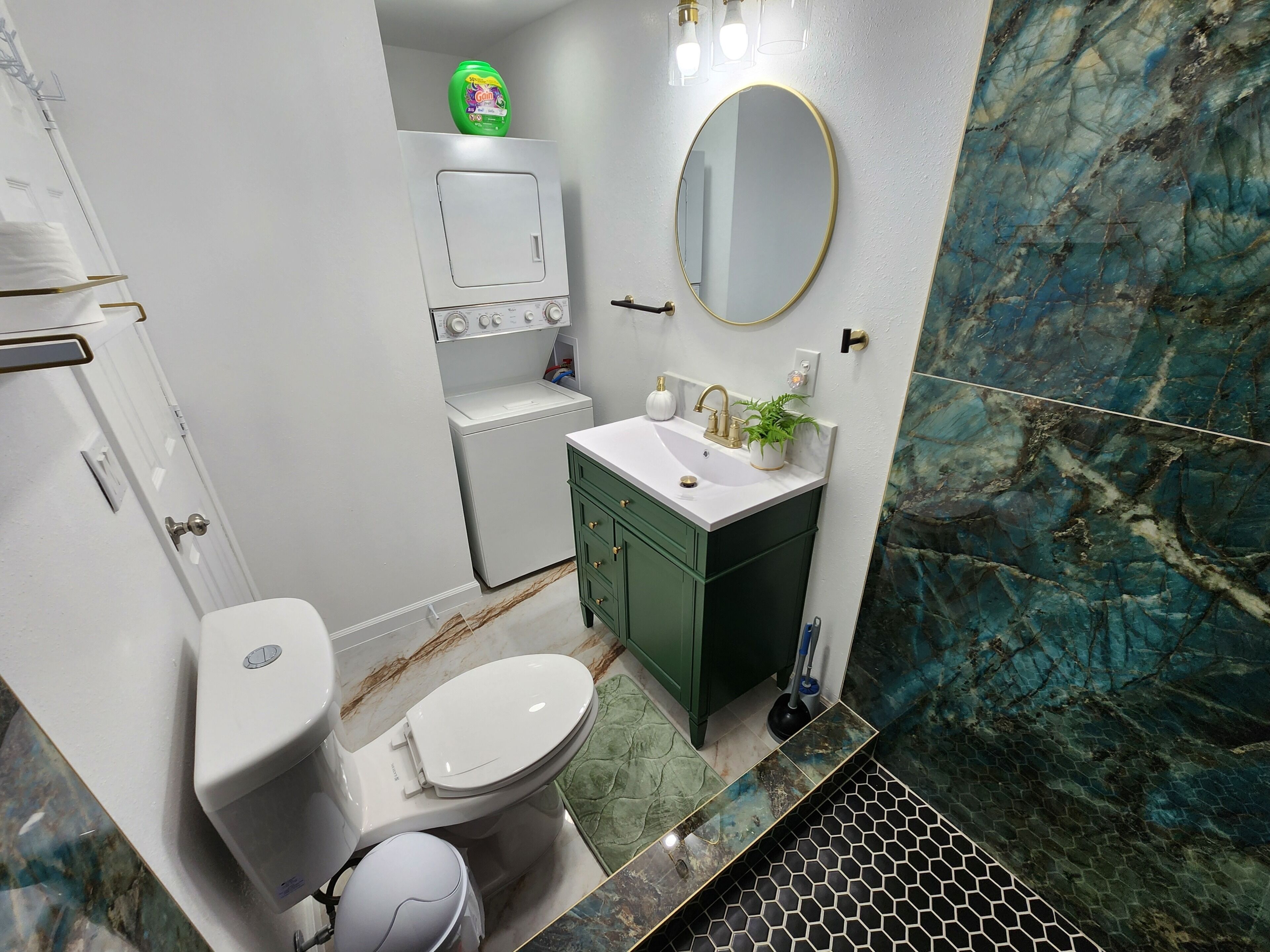 Une salle de bain comprenant des toilettes, un lavabo, des meubles verts, un miroir et un pare-feu en marbre.