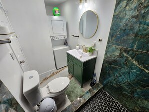 Un baño con inodoro, lavabo, armarios verdes, un espejo y un salpicadero de mármol.