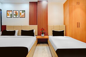 Ein Hotelzimmer mit zwei Betten, einem Holzschrank, einem Nachttisch mit Blumenvase und drei gerahmten Kunstwerken an der Wand.