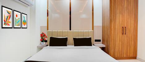 A modern hotel room with a large bed, a wooden wardrobe, and a wall-mounted air conditioner.
