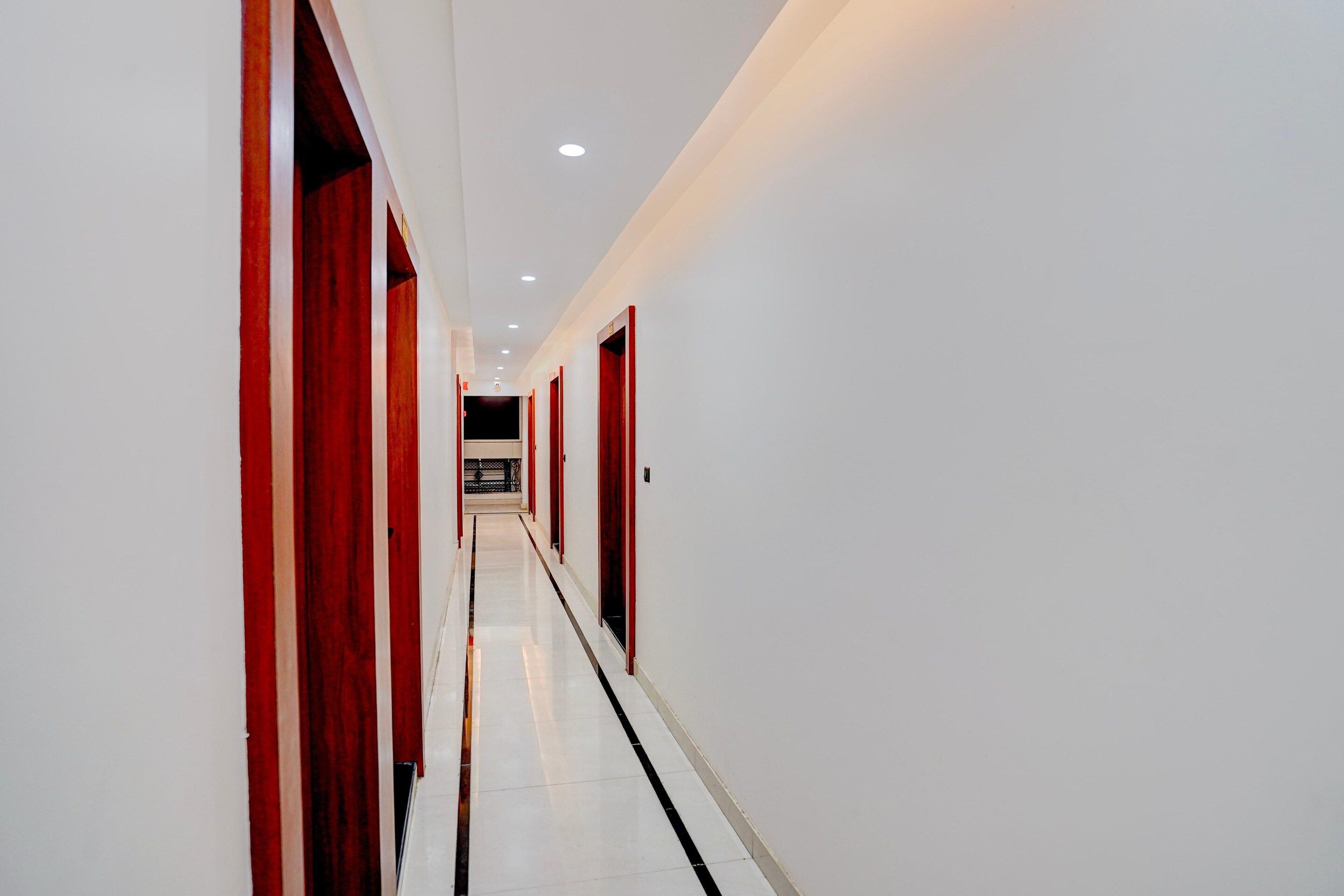 Un long couloir étroit aux murs blancs et aux touches de rouge, qui mène à une pièce sombre au bout.