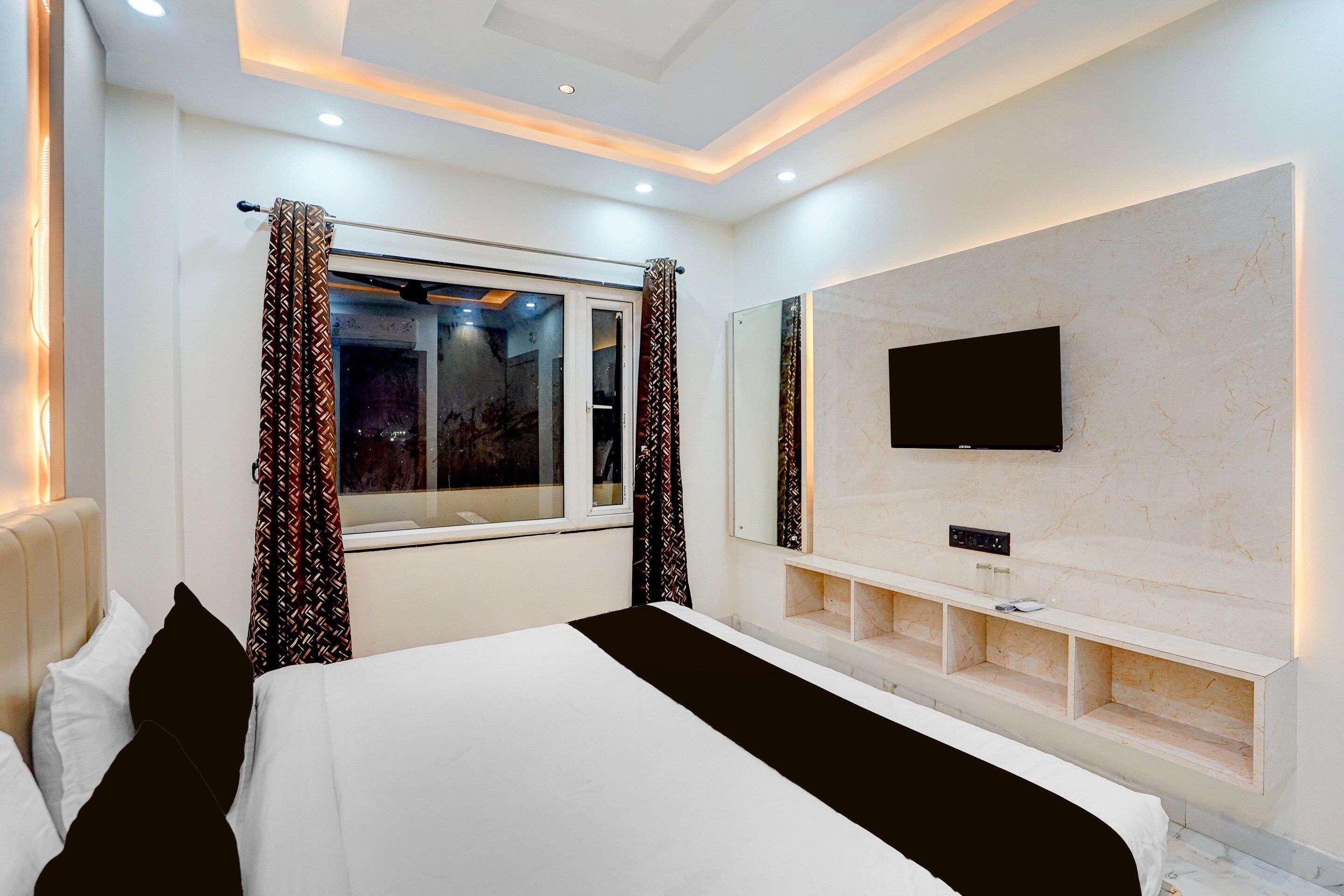 A modern hotel room with a large bed, a TV mounted on a marble wall, and a window with patterned curtains.
