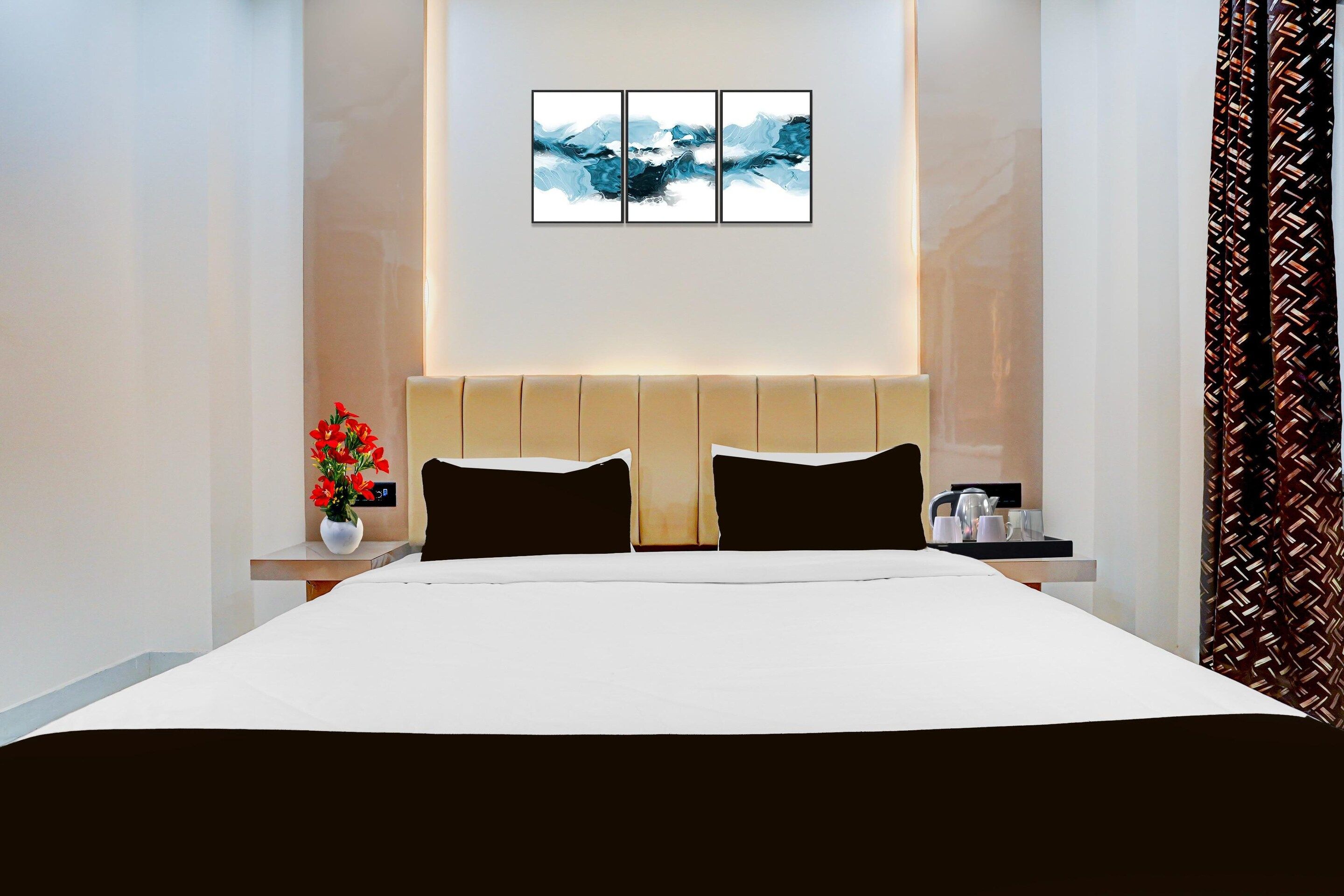 Una habitación de hotel con cama, mesita de noche, un jarrón con flores y un cuadro en la pared.