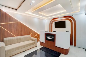 Ein Empfangsbereich mit modernem Design, inklusive einer Wand aus Holz, einem beigen Sofa und einem Empfangstisch mit der Beschriftung 'TOWNHOUSE OYO-Serviced'.