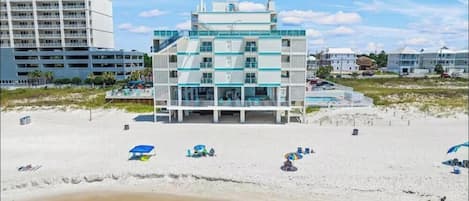 A beachfront hotel with multiple floors, a pool, and beach umbrellas.