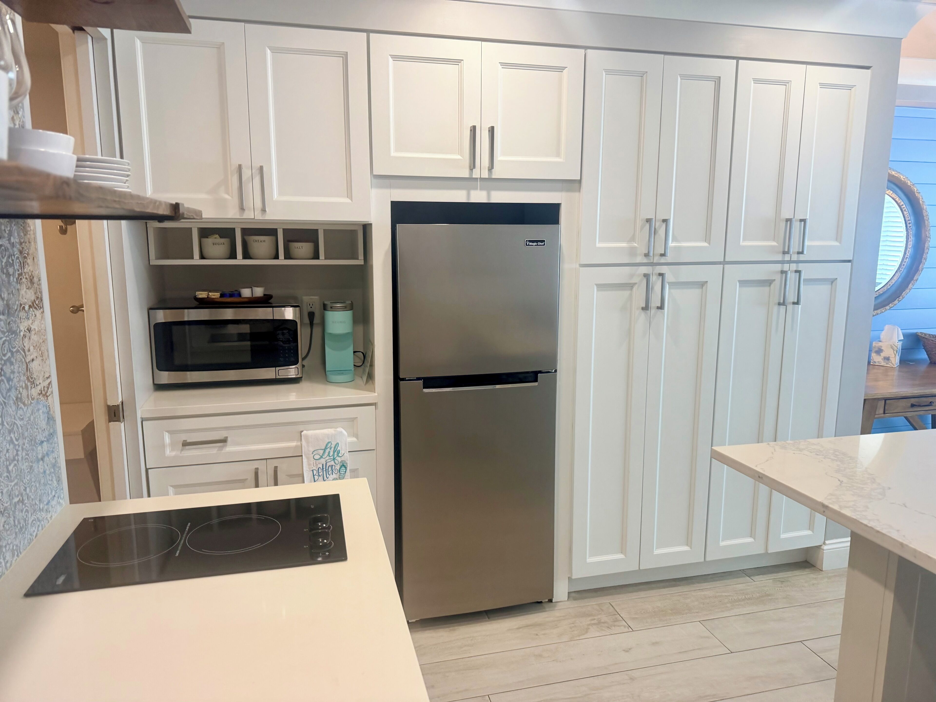 A modern kitchen with white cabinetry, a stainless steel refrigerator, a microwave, and an induction cooktop.