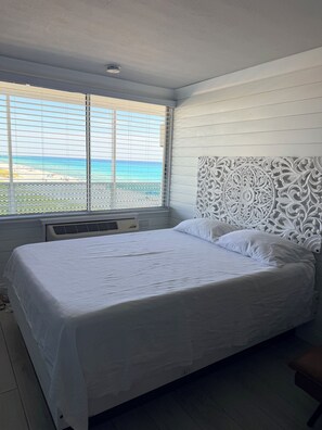 Ein Bett mit weißem Kopfteil und Blick auf den Strand durch ein Fenster.