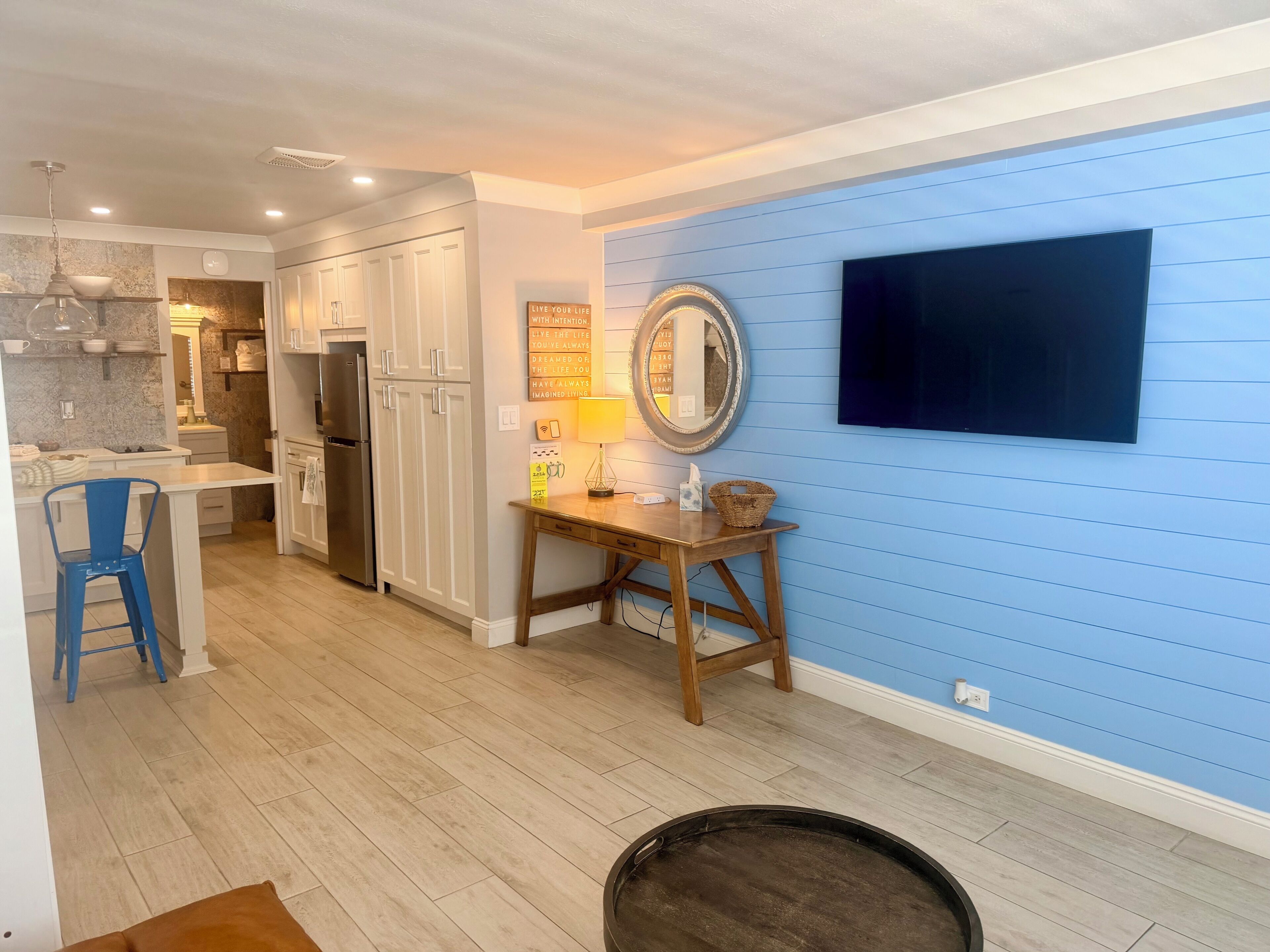 A kitchen with white cabinets, a blue wall, a wooden table, and a TV mounted on the wall.